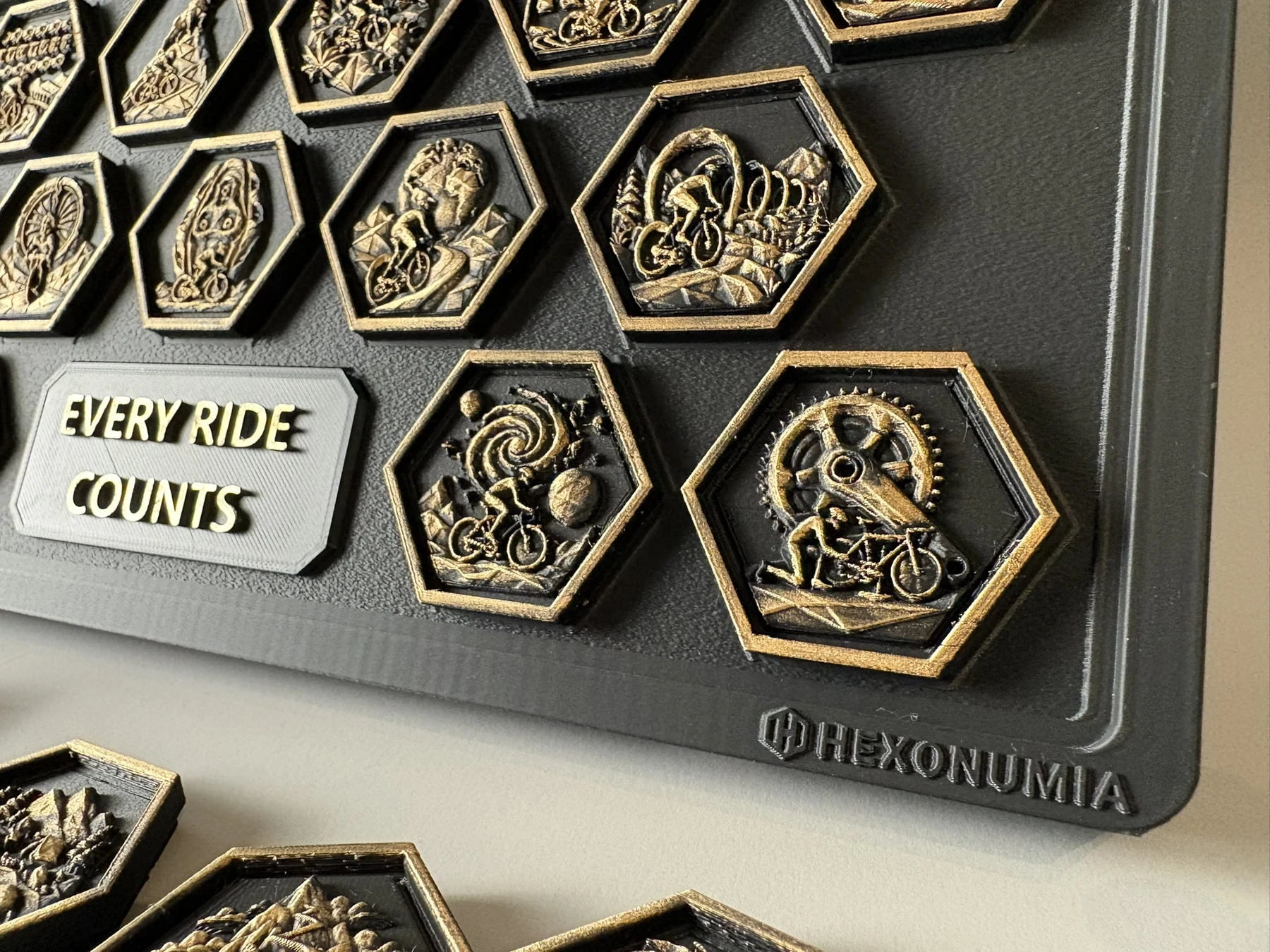 Close view of Hexonumia Cycling achievement pieces showing metallic relief, rim finish and board branding